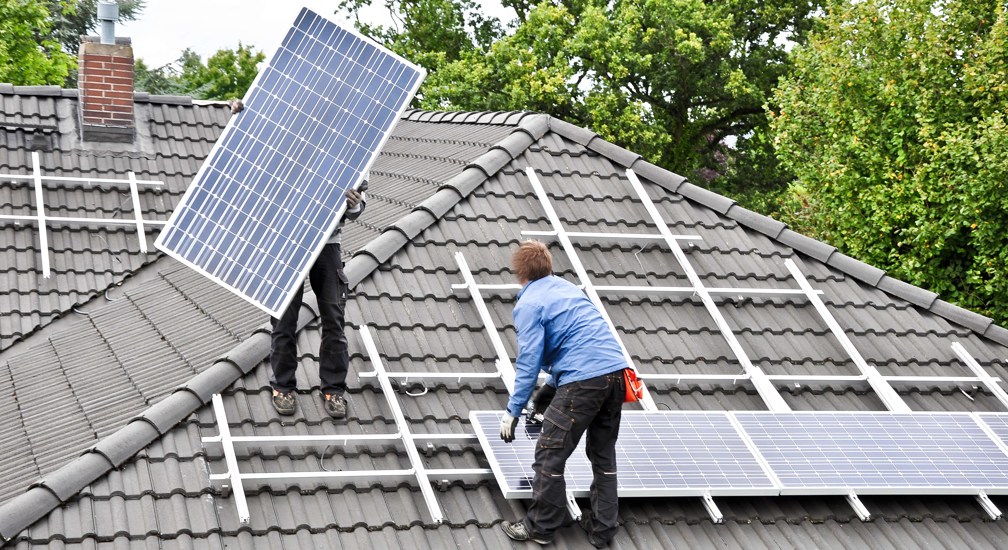 Handwerker montieren zwei Solarpanels auf ein Hausdach