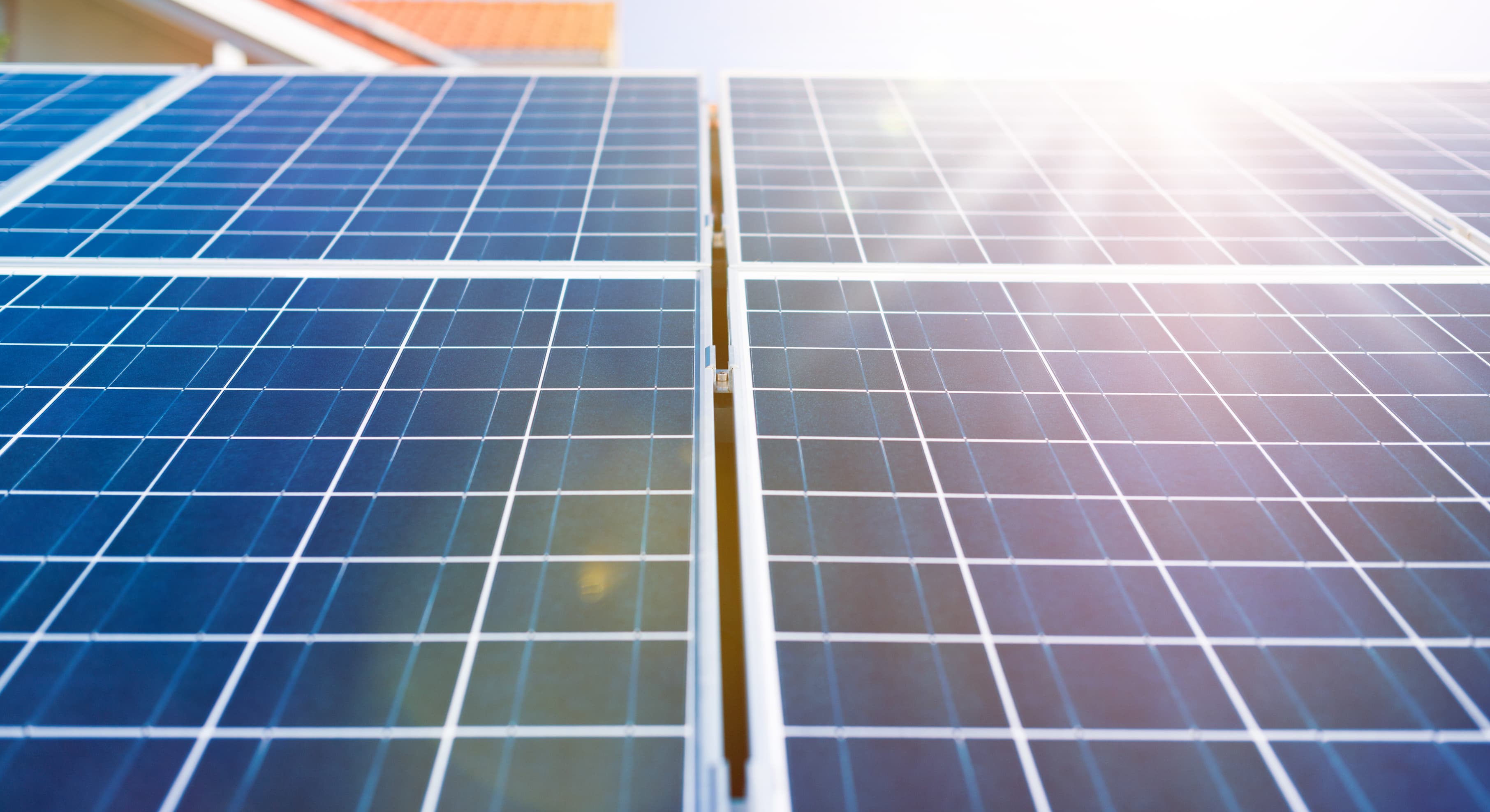 Nahaufnahme von blauen Solarmodulen mit einem klaren Rastermuster, beleuchtet von hellem Sonnenlicht. Die Module gehören zu einer Solaranlage auf einem Wohnhaus und erzeugen erneuerbare Energie zur nachhaltigen Stromversorgung.
