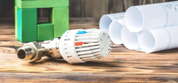 Thermostat neben Bauzeichnungen und grünem Haus