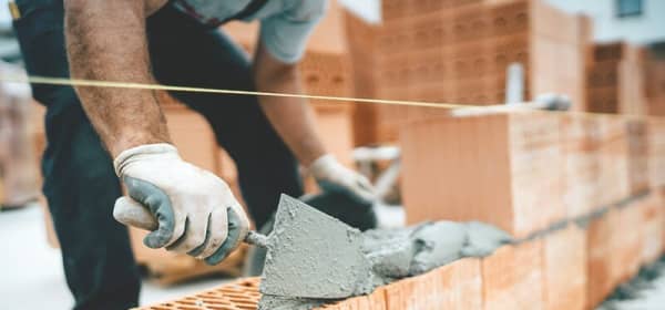 Maurer baut ein Massivhaus und streicht Zement auf Bausteine