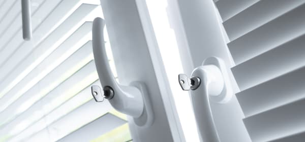 Zwei Fenster mit weißen Rollos und Sicherheitsgriffen, davon ist das linke gekippt