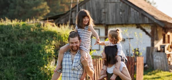 Junge Familie mit Mutter, Vater und zwei Kindern spazieren glücklich vor altem Haus