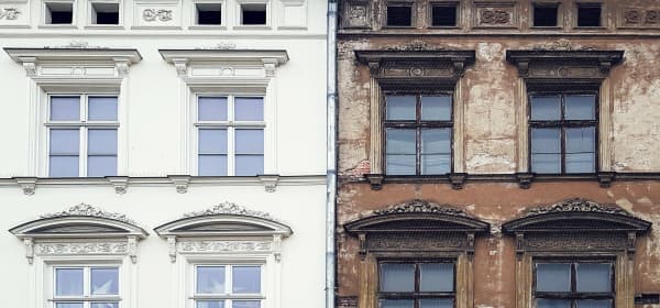frisch saniertes weißes Mehrfamilienhaus neben unsaniertem Haus mit brauner, bröckelnder Fassade
