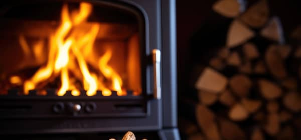 Holzpellets in Nahansicht vor einer Holzheizung mit Holzscheiten im Hintergrund