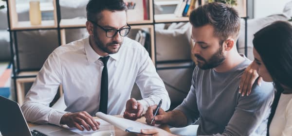 Immobilienmakler und junges Paar am Schreibtisch