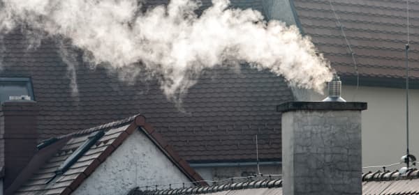 Schornstein mit Rauch vor grauen Wohnhäusern