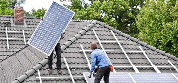 Handwerker montieren zwei Solarpanels auf ein Hausdach