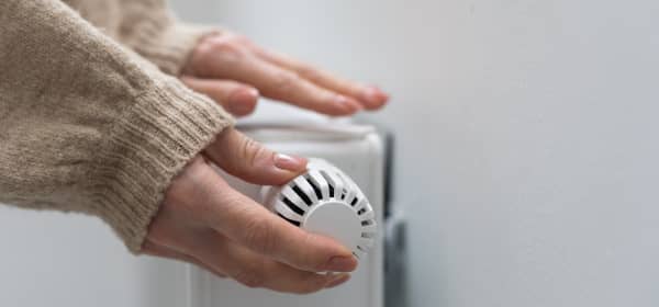 Eine Hand dreht die Heizung auf, die andere liegt auf dem Heizkörper und prüft, ob es warm wird