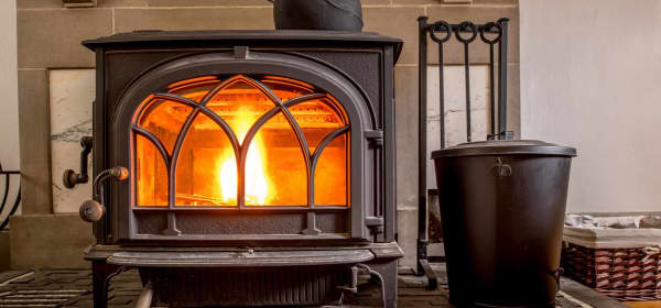 Moderner brennender Kaminofen aus Gusseisen im Wohnraum mit gusseisernem Teekessel zur Luftbefeuchtung oben auf dem Ofen