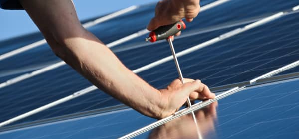 Zwei Hände montieren Solarmodule auf einem Dach