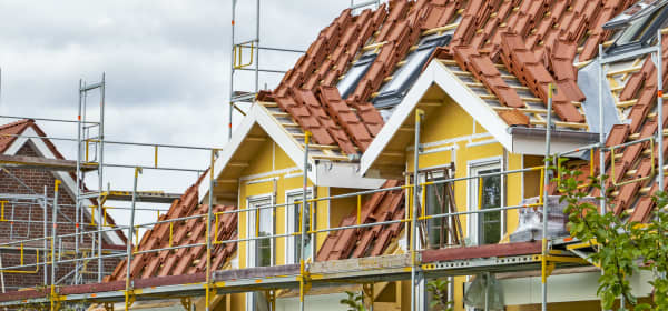 Gerüst an Wohnhaus mit gelber Fassade, dessen Dach neu gedeckt werden soll