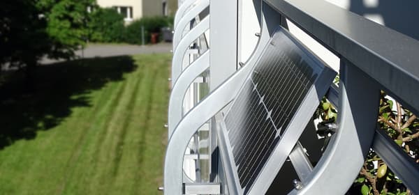 Seitenansicht eines Mehrfamilienhauses mit Balkonen, der Fokus liegt auf einem Solarmodul, das an einem der Balkone montiert ist