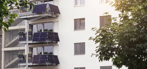 Mehrfamilienhaus mit heller Fassade und Balkonen, an denen jeweils mehrere Solarmodule installiert sind