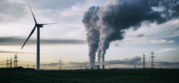 Windrad vor bewölktem Himmel, im Hintergrund Strommasten und ein Kraftwerk
