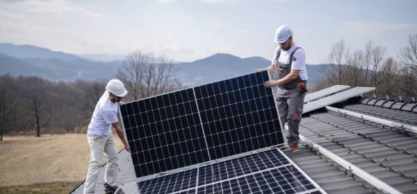 Zwei Installateure montieren ein Solarmodul auf ein Hausdach.
