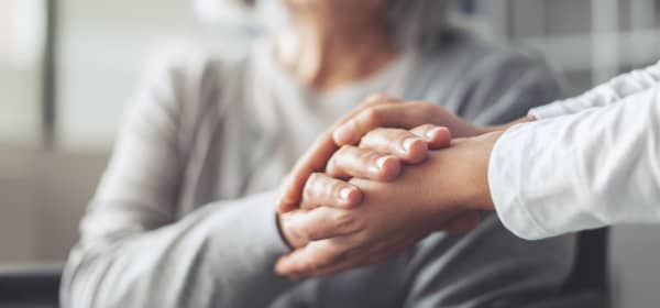 Seniorin und jüngere Person halten sich die Hände