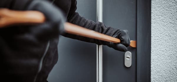 Dunkel gekleideter Einbrecher stemmt eine schwarze Haustür mit einem Brecheisen auf