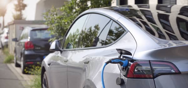 Silbernes Elektroauto am Straßenrand mit eingestecktem Ladestecker
