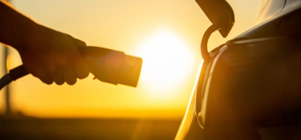 Person steckt bei Sonnenuntergang einen Ladestecker in ein E-Auto