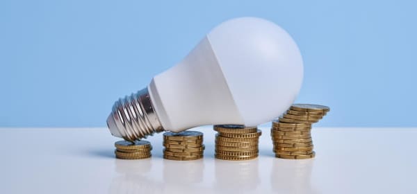 Glühbirne auf aufgetürmten Münzen simuliert ein Wachstumsdiagramm
und verdeutlicht die steigenden Strompreise