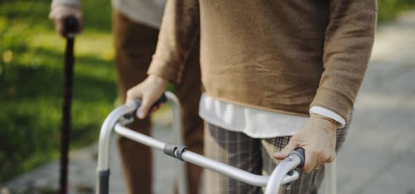 Senior und Seniorin mit Gehhilfe auf gepflastertem Weg