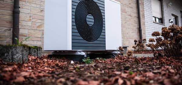 Luftwärmepumpe im Herbst vor einem Wohnhaus mit hellbrauner Steinfassade