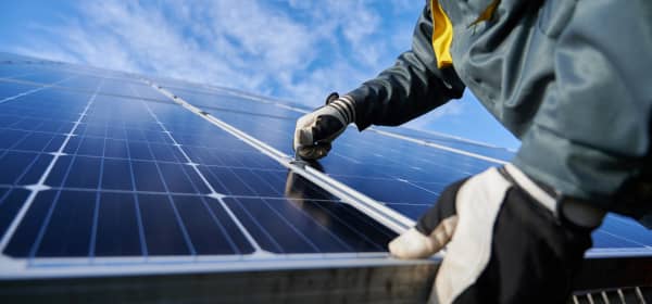 Nahaufnahme eines Arbeiters mit Handschuhen, der an einem installierten Solarmodul auf einem Dach arbeitet