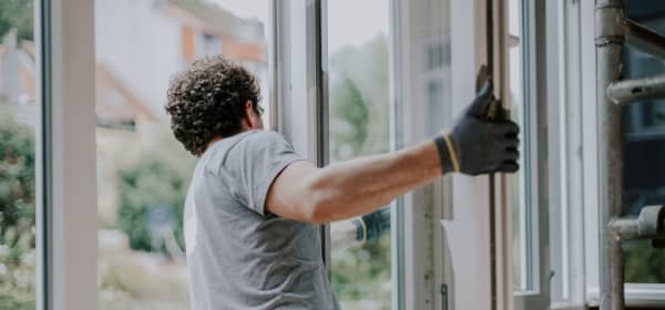 Handwerker hängt den Flügel eines Fensters in einem sanierungsbedürftigen Wohnraum aus