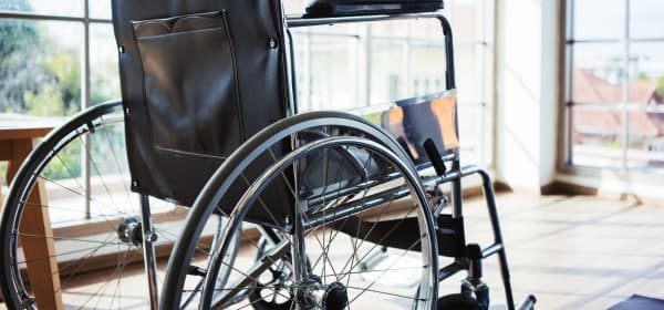 Rollstuhl in einem leeren, hellen Raum mit bodentiefen Fenstern