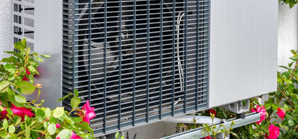 Nahaufnahme einer Wärmepumpe an einem Gebäude von Blumen umgeben