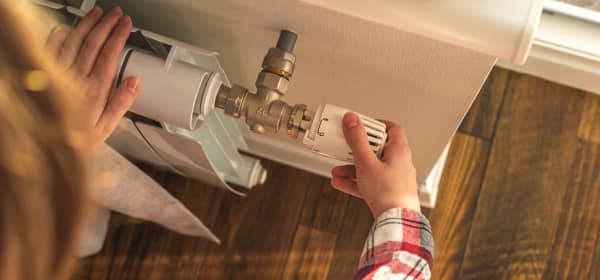 Person dreht das Thermostat eines Heizkörpers