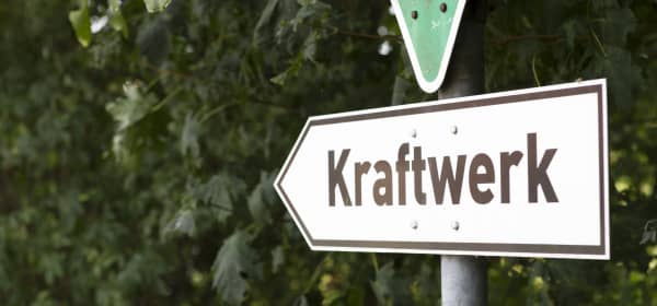 Richtungsweisendes Schild mit der Aufschrift Kraftwerk vor grünen Büschen