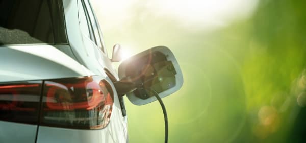 Weißes Elektroauto vor grünem Hintergrund wird geladen