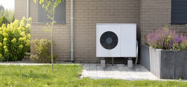 Weiße Luft-Wärmepumpe vor Hausfassade mit braunen Ziegeln
