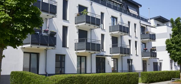 Modernes Mehrfamilienhaus mit weißer Fassade und Balkonen, davor eine gepflegte, grüne Hecke