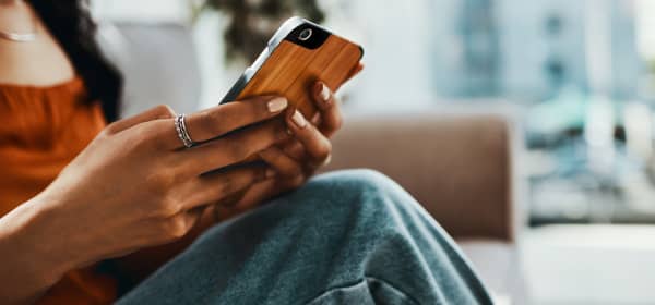 Junge Frau mit Smartphone in der Hand sitzt in Wohnung