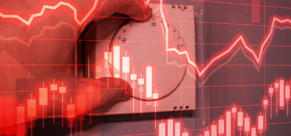 Hand dreht an Wandthermostat für eine Heizung mit grafischer Darstellung der Energiepreise