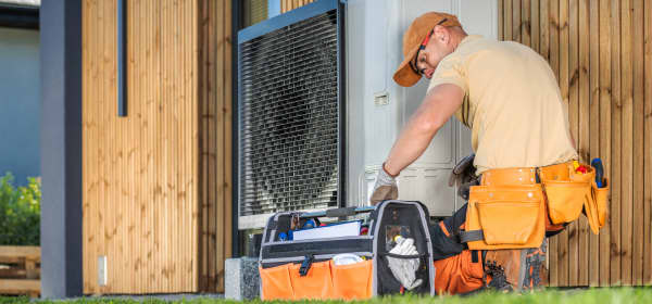 Monteur arbeitet an einer Wärmepumpe, die an einer Hausfassade steht