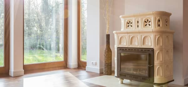 Cremefarbener Kaminofen in einem lichtdurchfluteten Wohnzimmer mit bodentiefen Holzfenstern