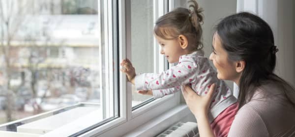 Mutter und Kleinkind schauen aus einem Fenster in einer Wohnung