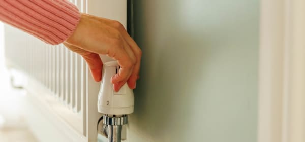 Frauenhand, die das Thermostatventil an einem Heizkörper einstellt.