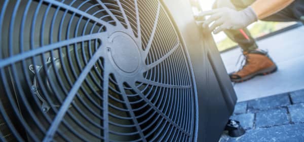 Ein Techniker führt Wartungsarbeiten an einer Klimaanlage auf einem Dach durch. Die Sonne scheint hell im Hintergrund