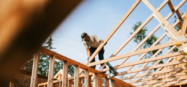 Mann auf dem Dachstuhl eines Rohbaus in Holzbauweise