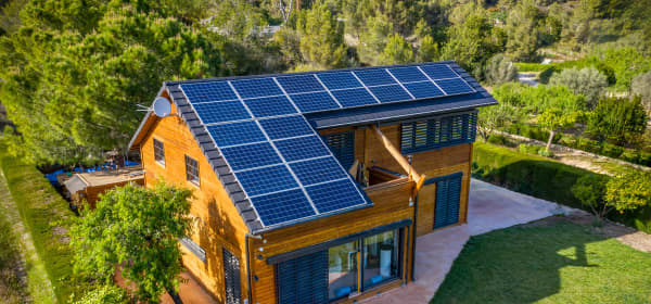 Photovoltaik-Paneele auf einem Holzhausdach umringt von grünem Garten