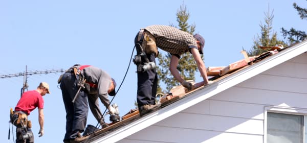 Drei Handwerker machen eine energetische Sanierung auf einem Hausdach