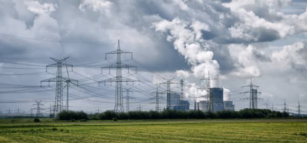 Laufendes Kraftwerk und Strommasten mit grüner Wiese im Vordergrund