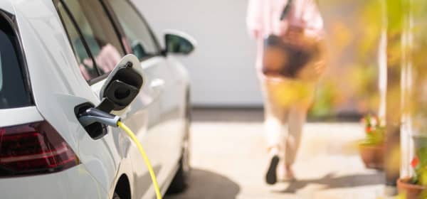 Weißes Elektroauto, das gerade geladen wird, mit weiblicher Silhouette im Hintergrund