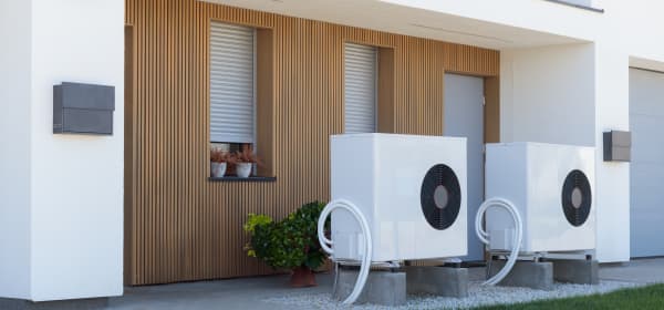 Zwei weiße Luftwärmepumpen vor modernem Wohnhaus mit Holzfassade