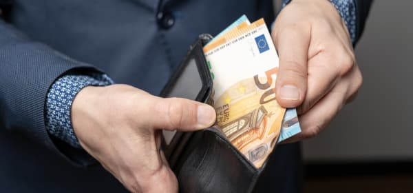 Älterer Mann im Anzug öffnet eine Geldbörse mit mehreren Geldscheinen