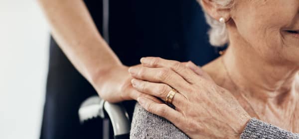 Junge Frau legt eine Hand auf die Schulter einer Seniorin in einem Rollstuhl